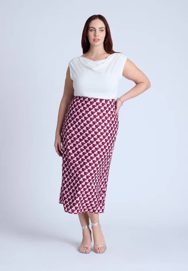 Person in a white top and patterned skirt stands confidently in sandals, posing for a fashion-related article