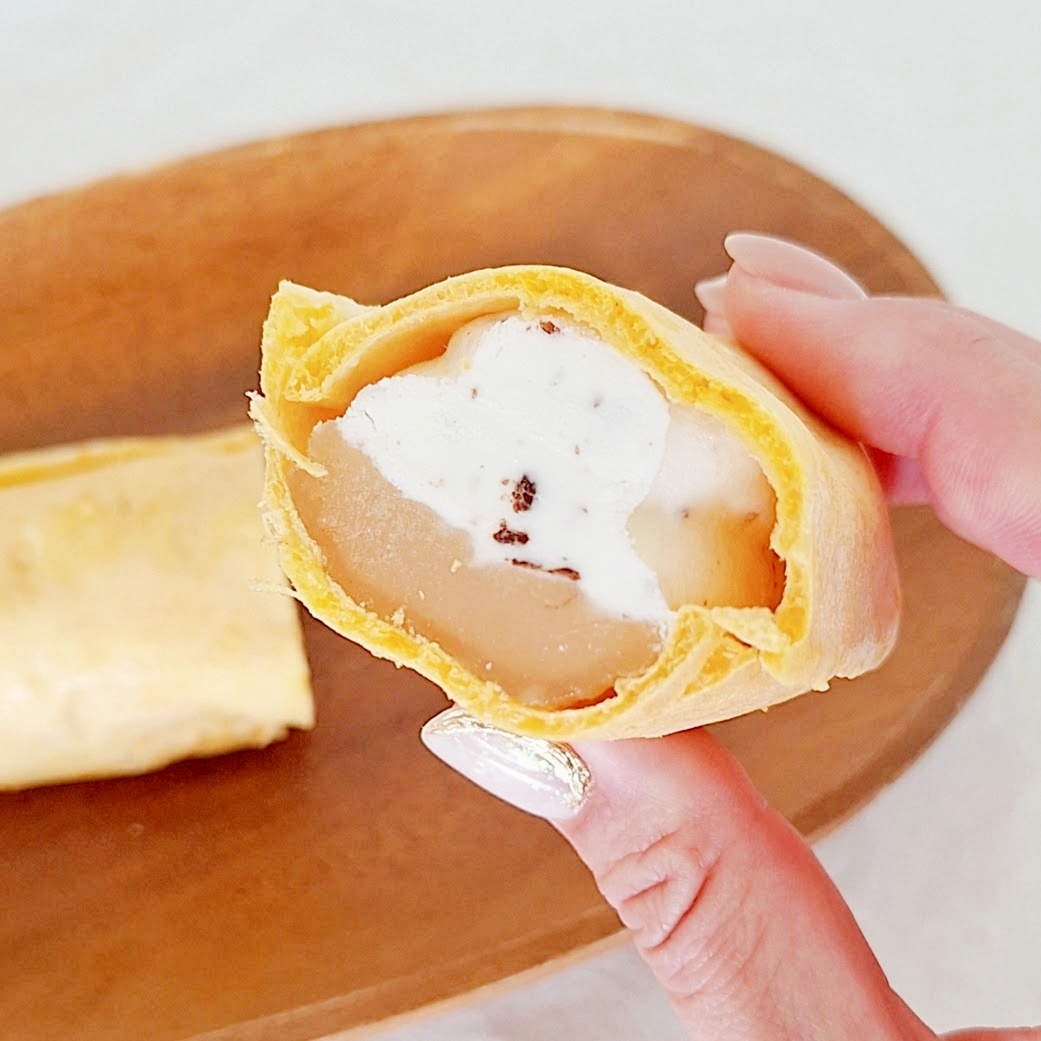 手に持った切られたクレープ、中にクリームとフルーツ。背景に木製プレートの上の別のクレープ。