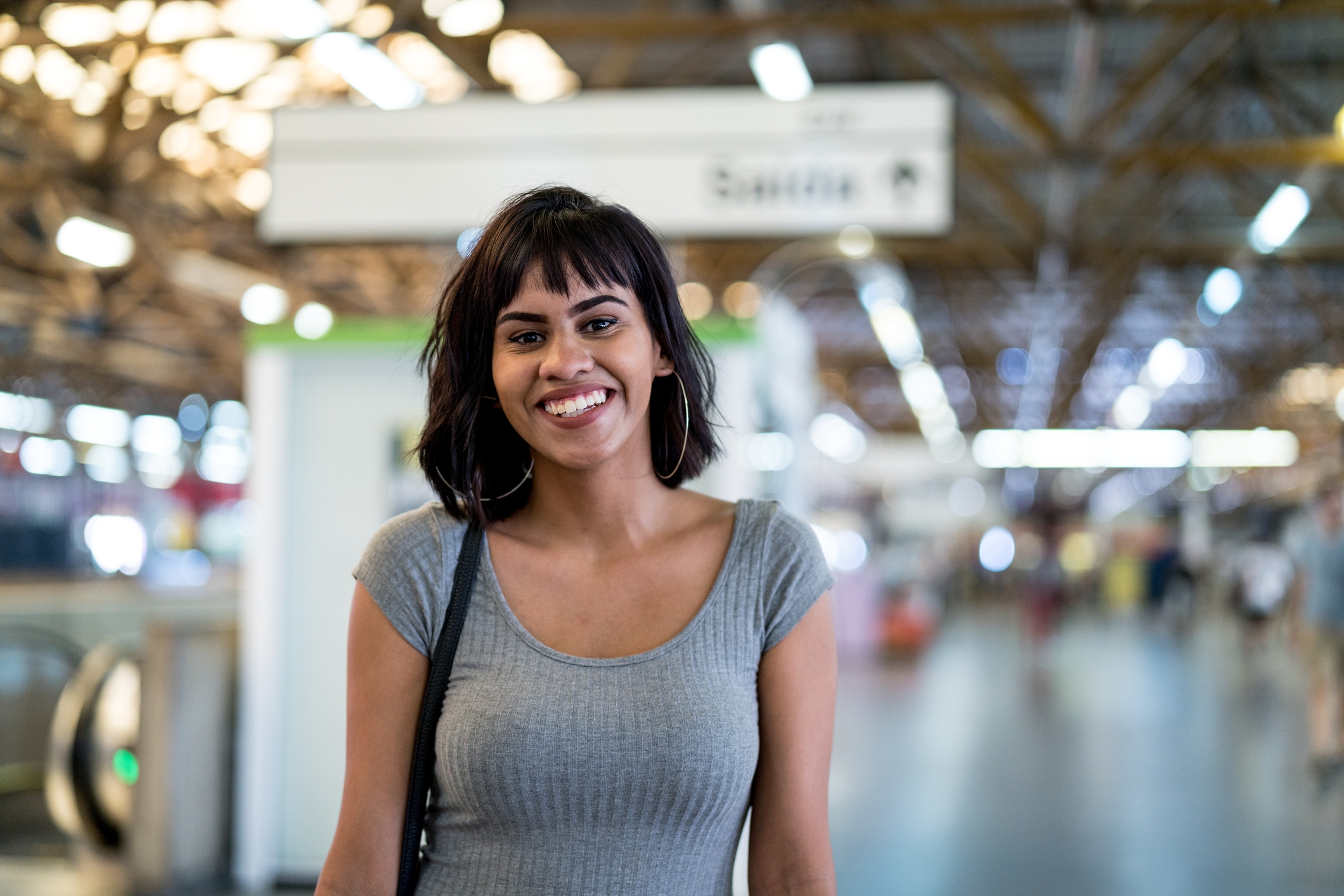 Person smiling in a busy indoor environment with blurred background activity