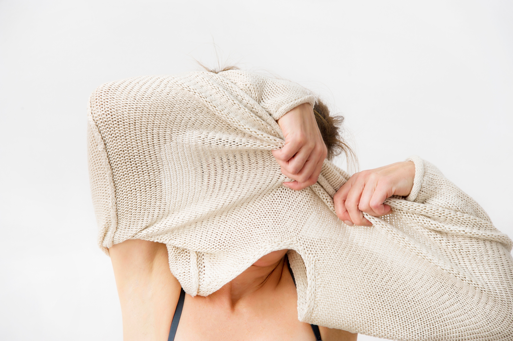 Person playfully hiding their face with a knitted sweater, arms raised. Casual and light-hearted moment