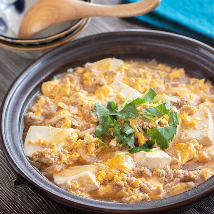 土鍋に豆腐、ひき肉、卵、パクチーが盛られた料理。豊かな香りが感じられそうな見た目です。