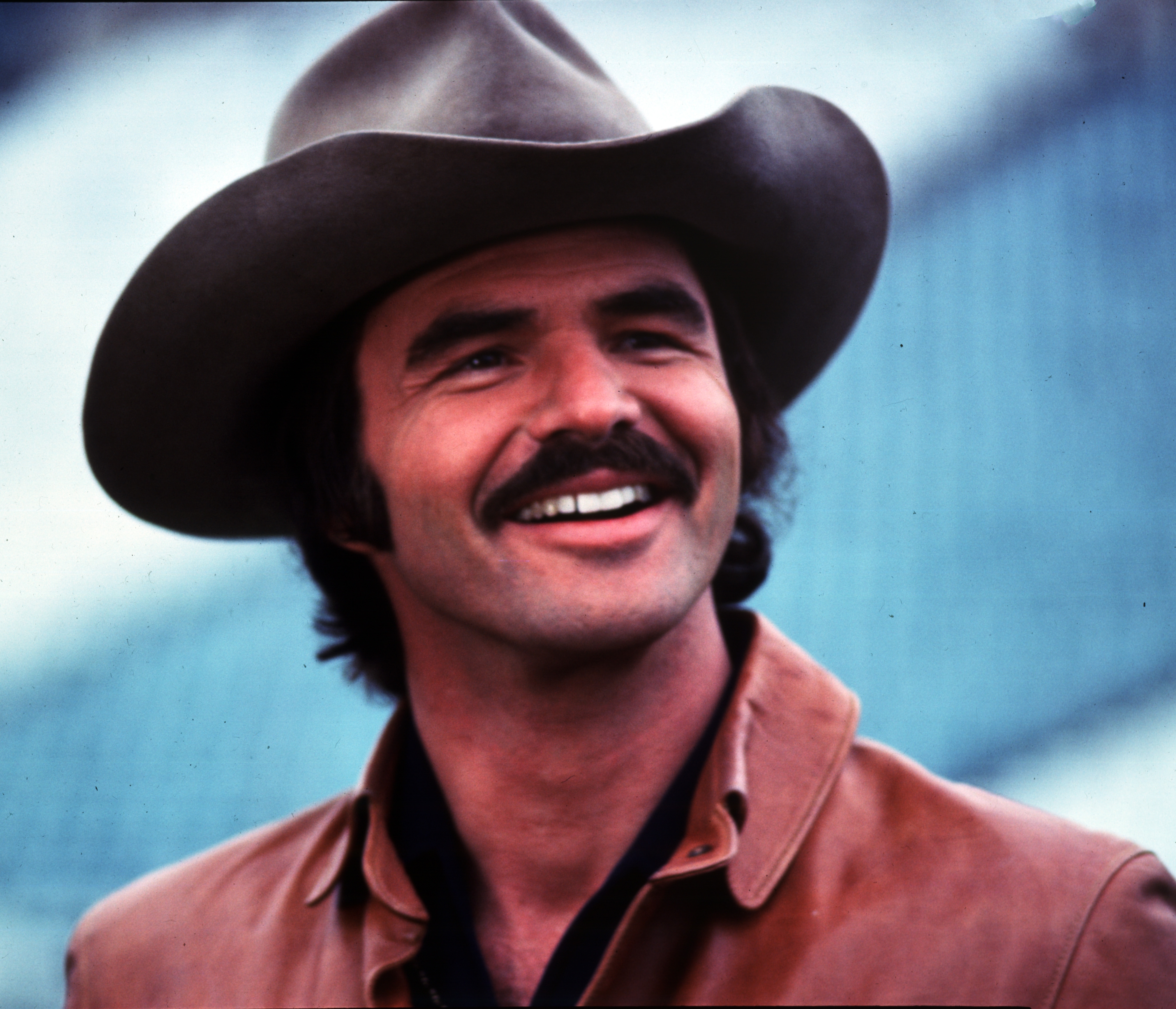 A person wearing a cowboy hat and leather jacket, smiling broadly