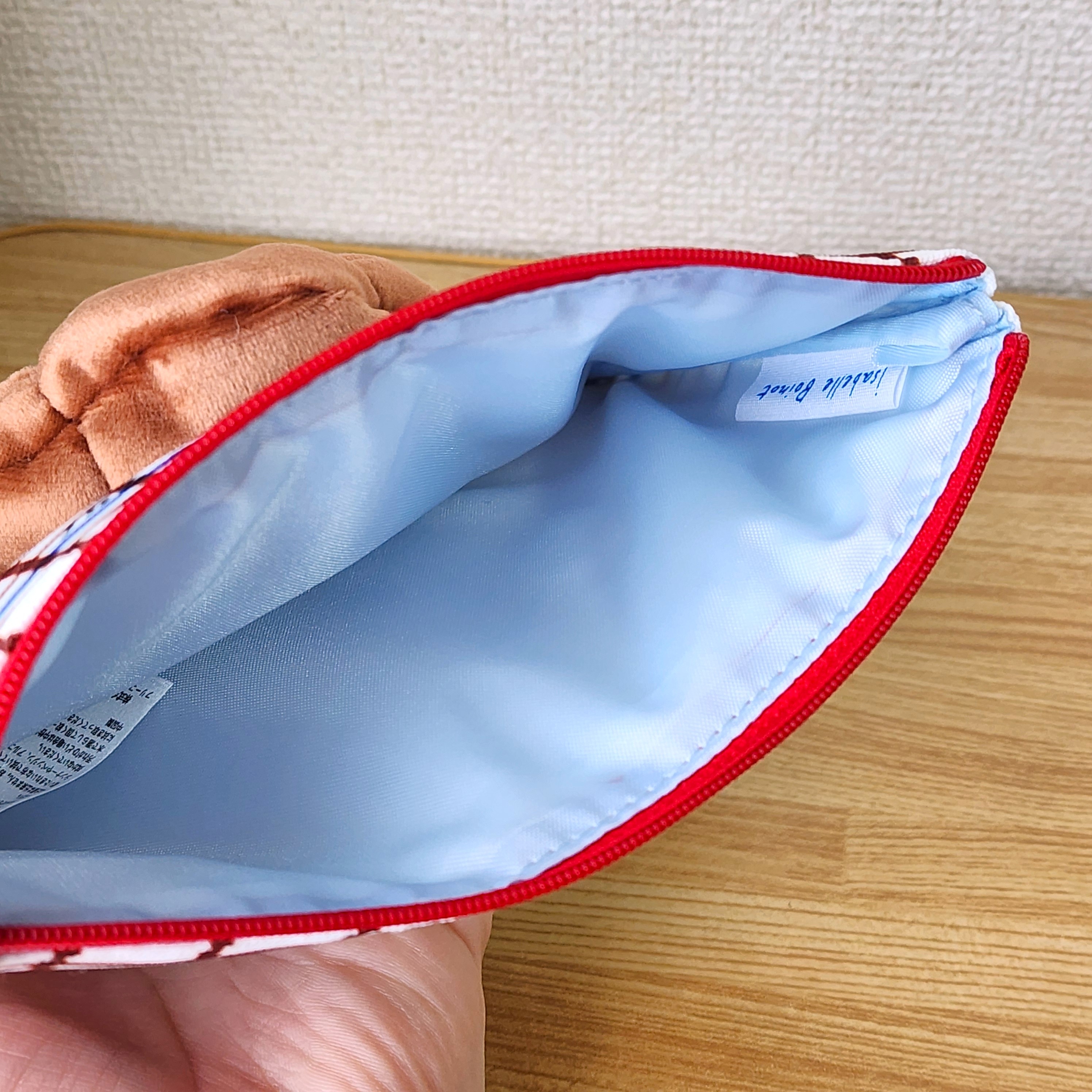ぬいぐるみが付いたポーチがテーブルに置かれている。開いた口から見える内側はシンプルなデザイン。
