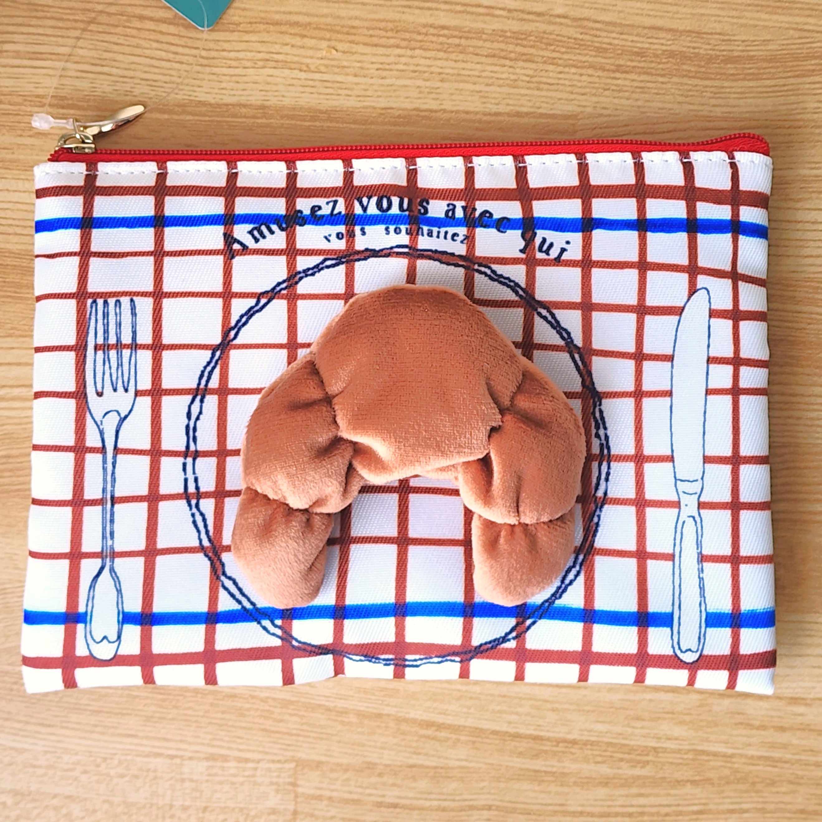 クロワッサン型のクッションが付いた、おしゃれなファスナーバッグ。食器が描かれた背景。