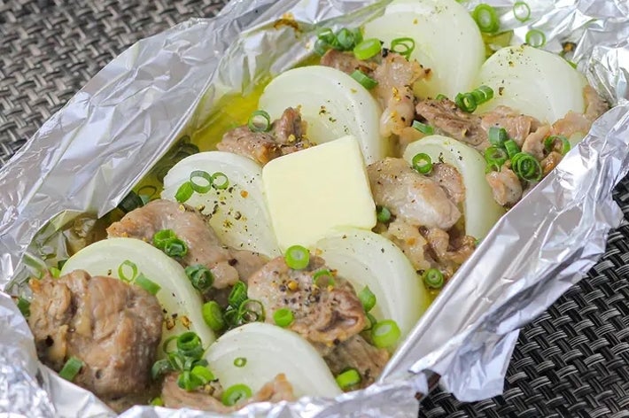 ホイルに包まれた調理済みの肉と玉ねぎ、バターとネギが添えられている料理。