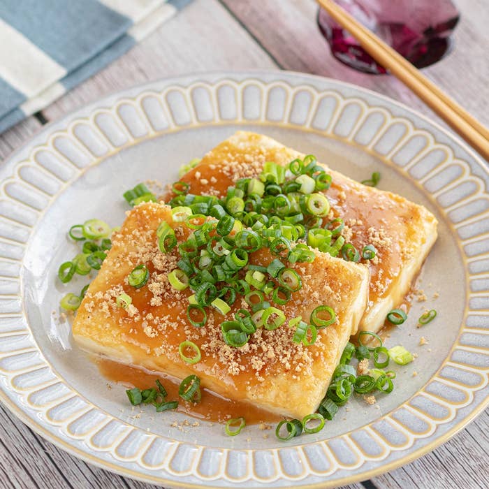 皿に盛られた揚げ豆腐にネギとソースがかかっている料理。食卓には箸が添えられている。