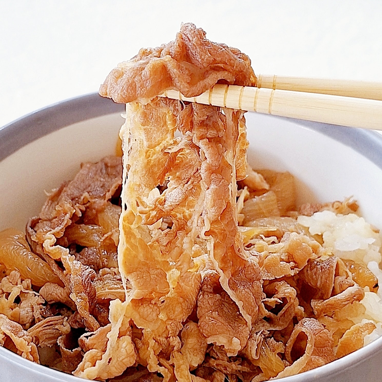 牛丼が盛り付けられた器から箸で持ち上げられる薄切り牛肉。
