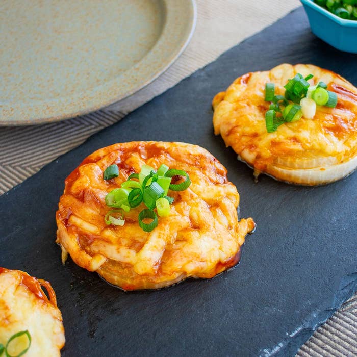 スレートプレートに盛られた、青ネギで飾られたチーズとソースのオニオンスナック。