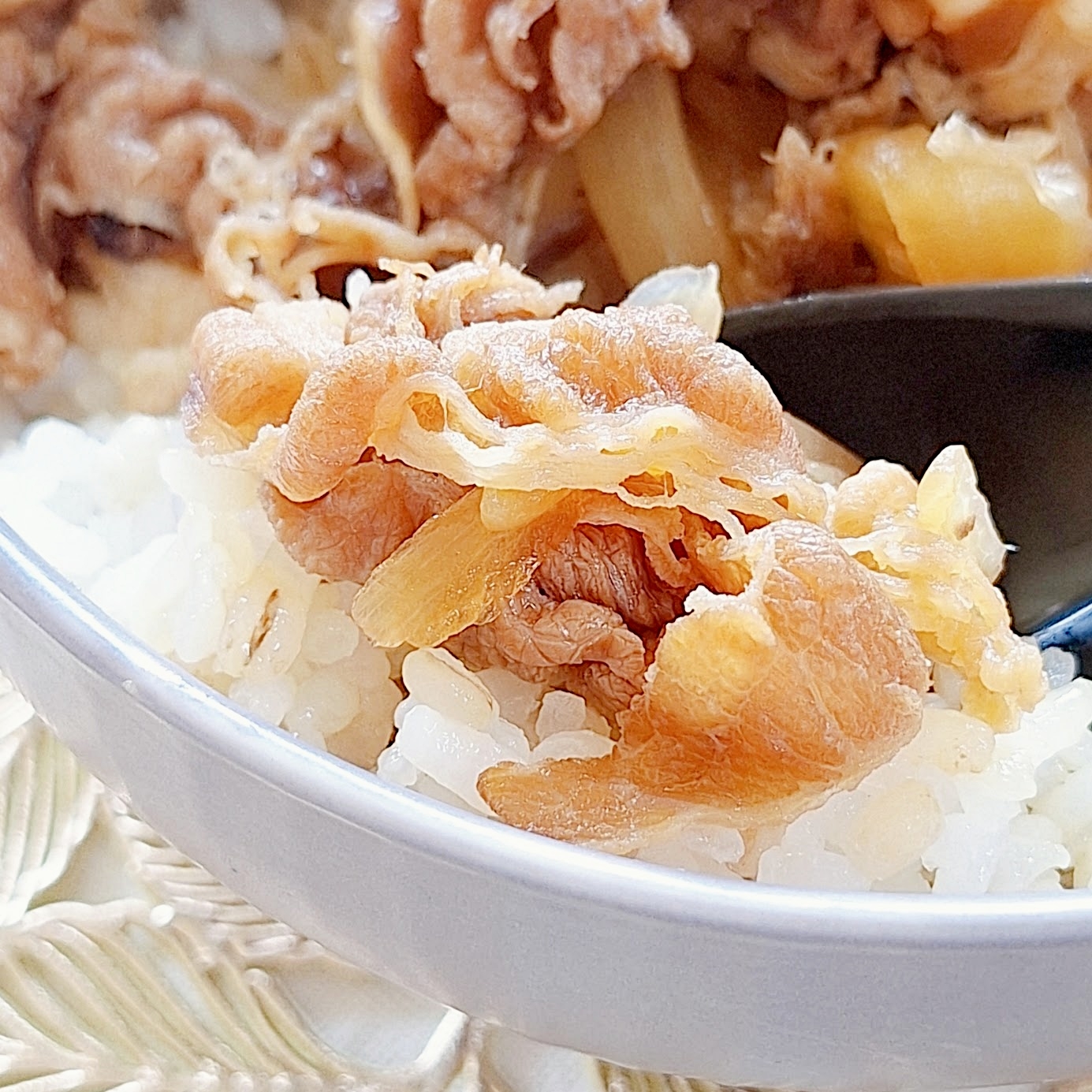 牛丼のクローズアップ画像。ご飯の上に牛肉と玉ねぎが盛られており、スプーンが添えられている。