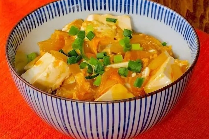 器に盛られた豆腐と野菜の料理。小口切りのネギが上に散らされている。赤い布の上に置かれている。