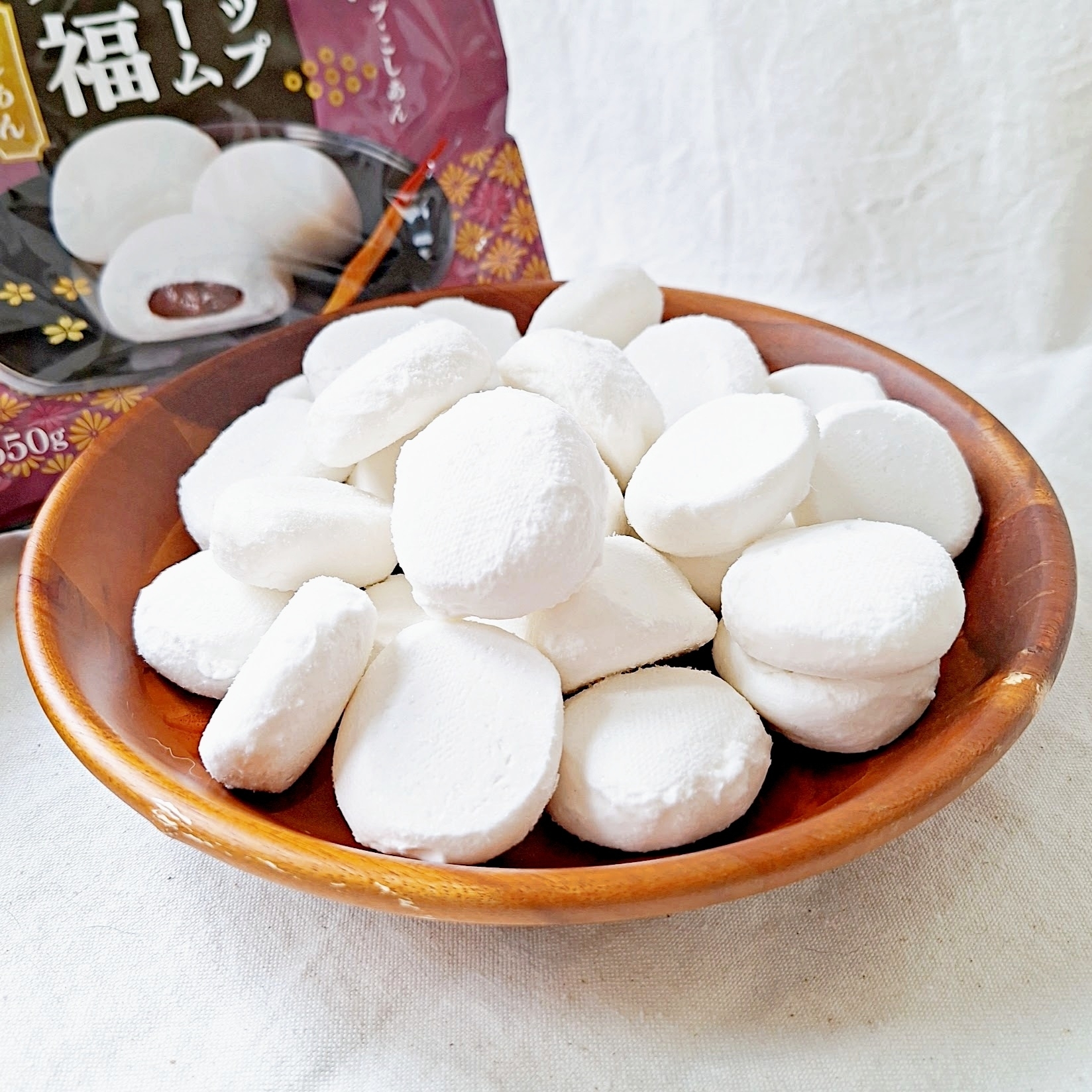 木のボウルに盛られた丸いマシュマロのようなお菓子が映っている。背景に商品のパッケージが見える。