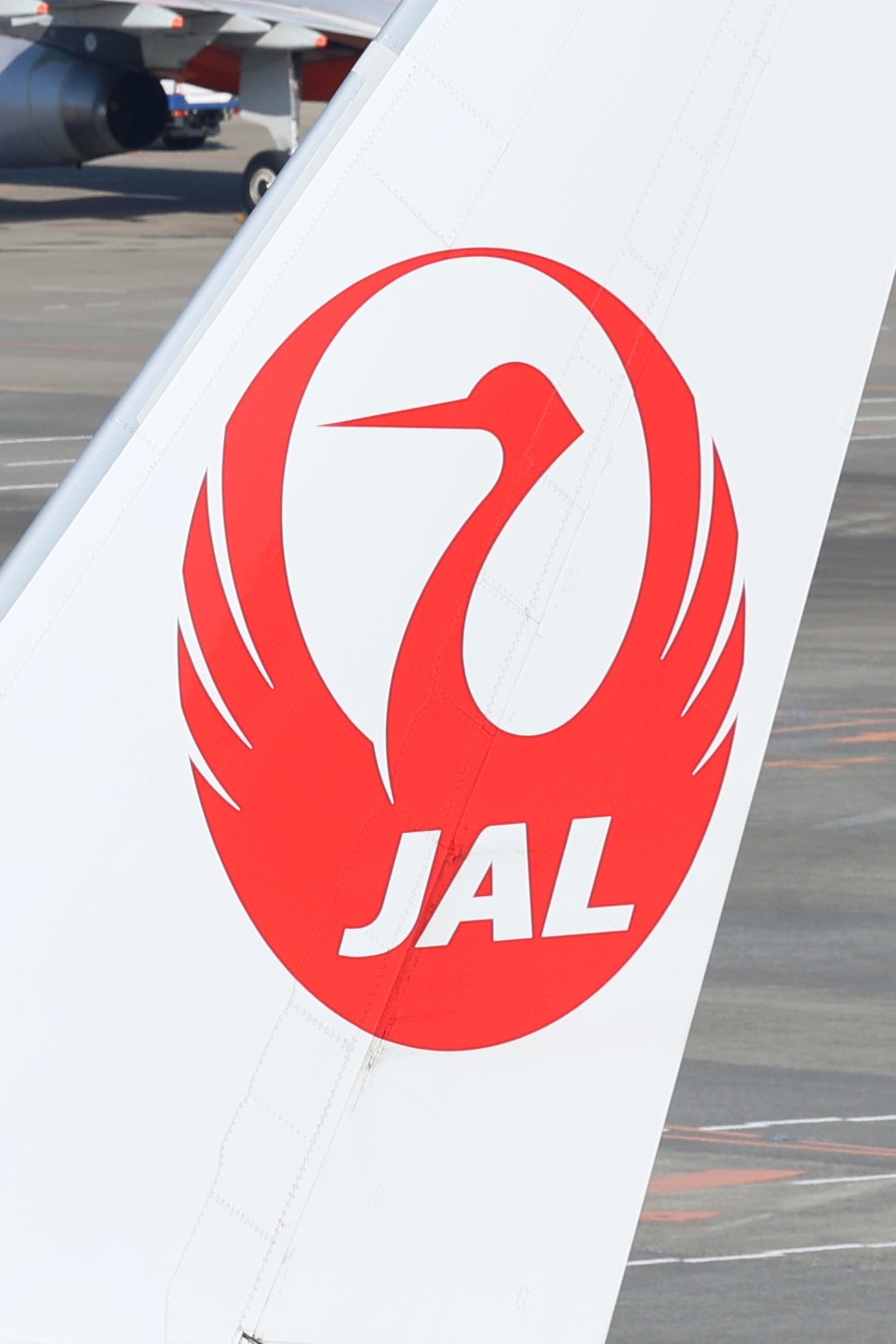 JALの飛行機の尾翼に描かれた鶴のロゴマークが空港の背景に映されている。
