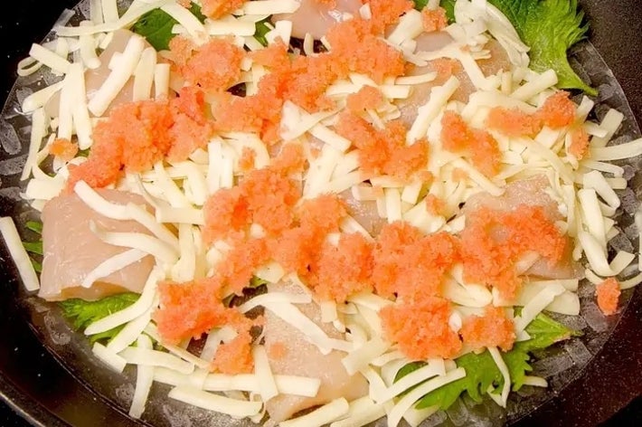 鍋の中で調理されている、チーズと魚卵がのった魚料理。青じそも見える。