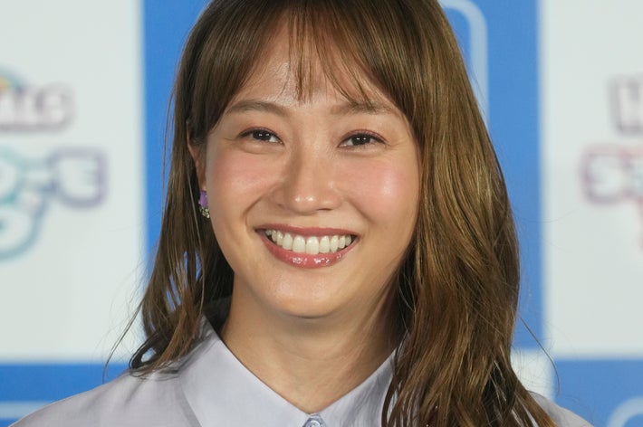 女性が微笑んでいる。シャツを着ており、背景にイベントのロゴがある。