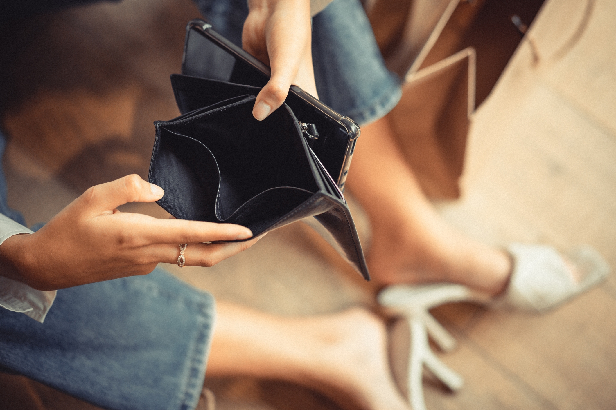 Person sitting on the floor, holding open an empty wallet, with casual shoes and jeans visible