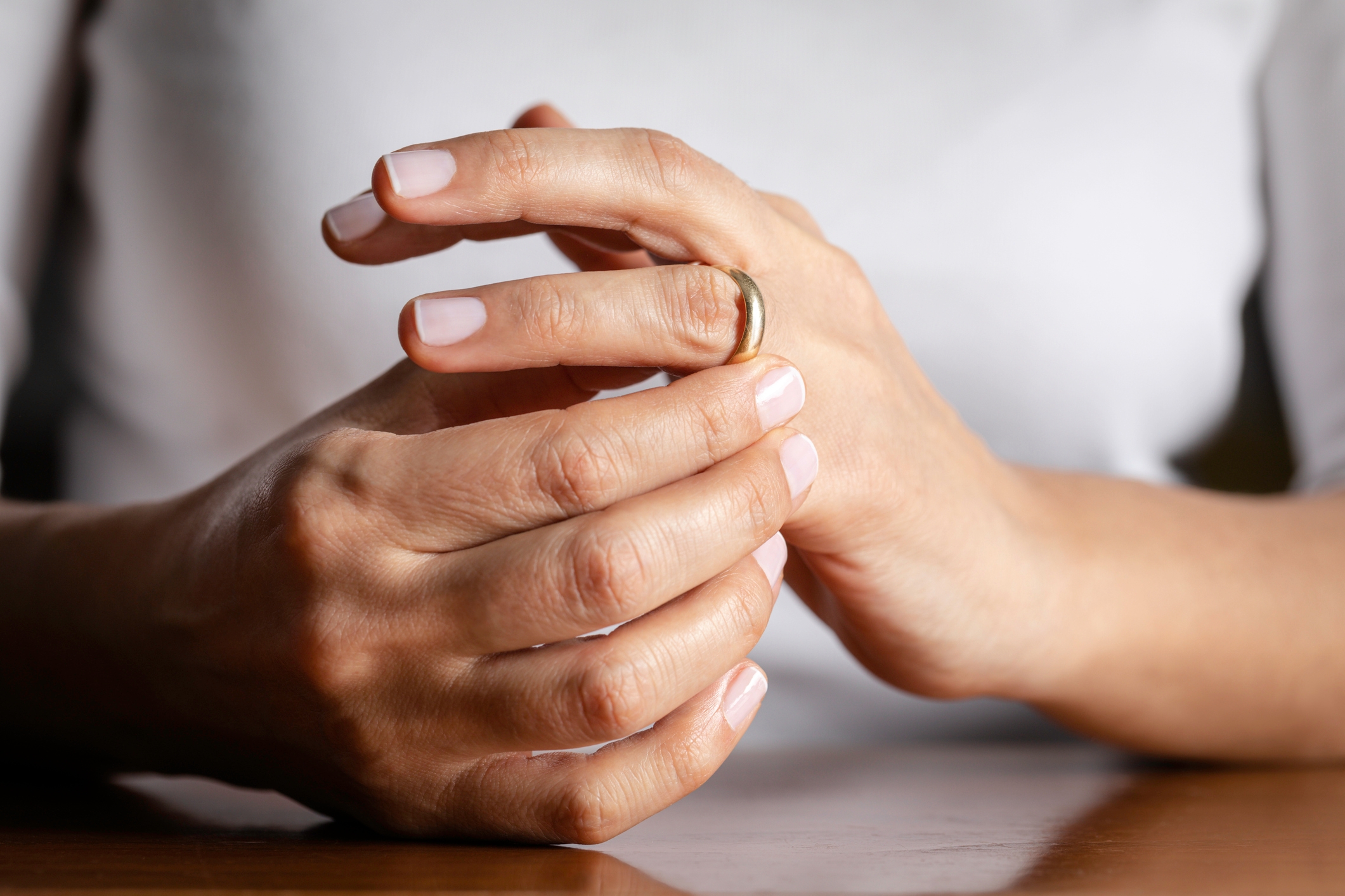 Person's hands touching a ring on their finger, suggesting contemplation or decision. They have neatly manicured nails