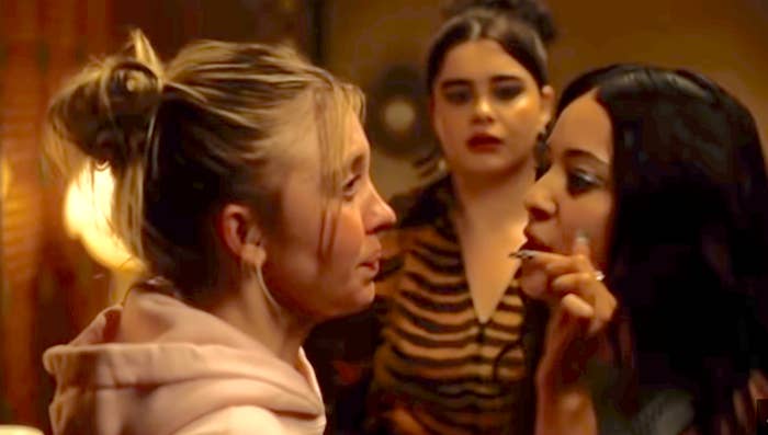 Three people in a tense scene; the woman on the right is pointing while the other two watch closely. Mood is intense and confrontational