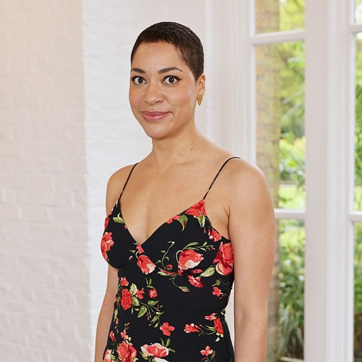 Person in a floral, sleeveless dress standing indoors with a neutral expression