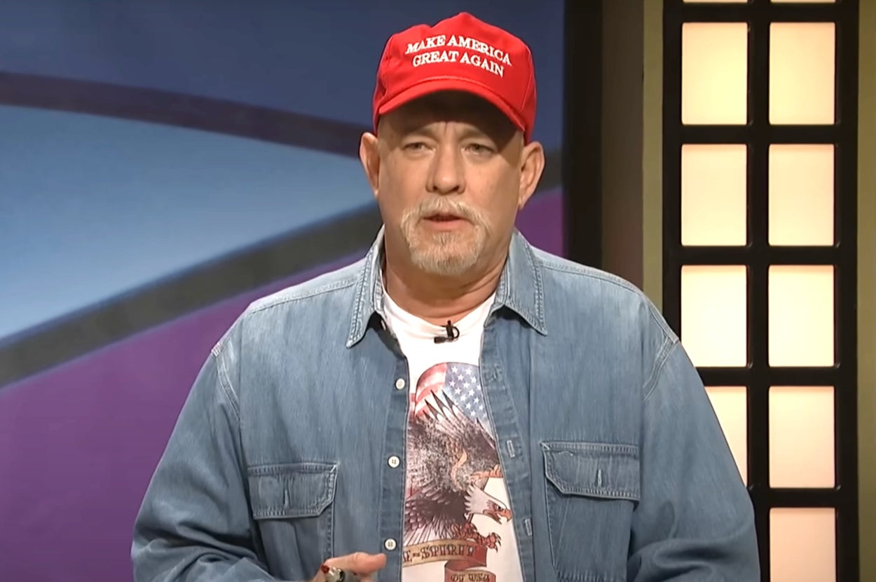 Man in a denim shirt and "Make America Great Again" hat speaks on stage, wearing a shirt with an eagle print