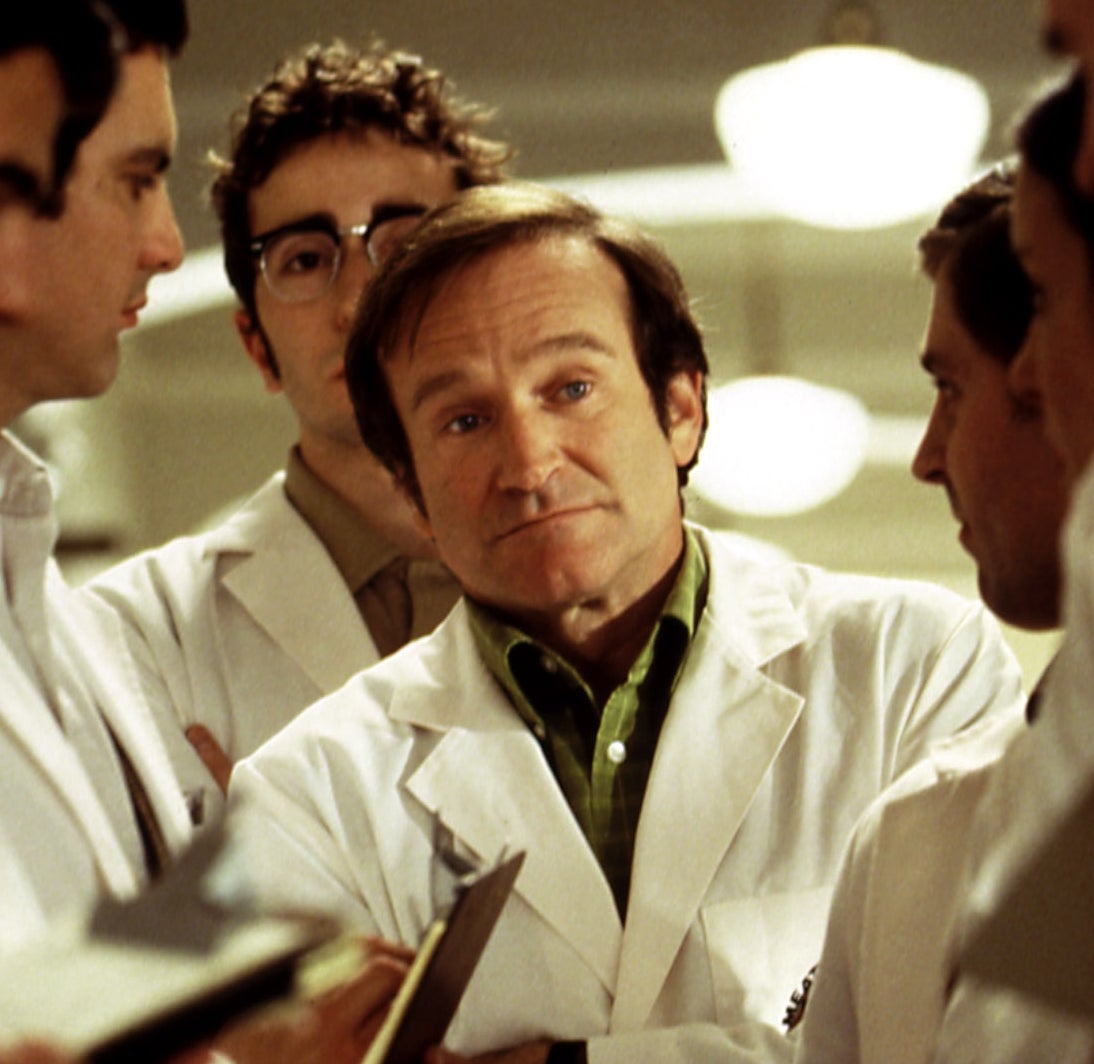 A person in a white lab coat stands among a group of others in similar attire, appearing thoughtful and engaged in a discussion