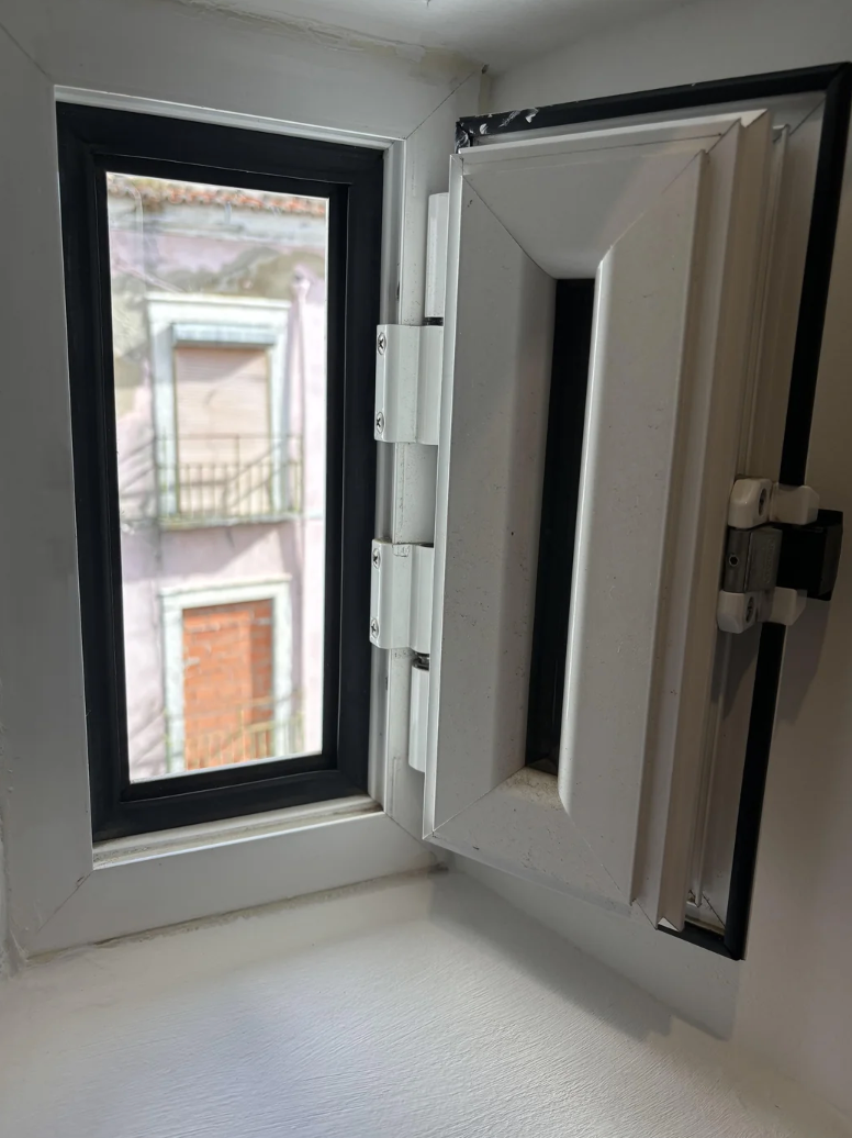 A small, open window with a view of a neighboring building and a balcony