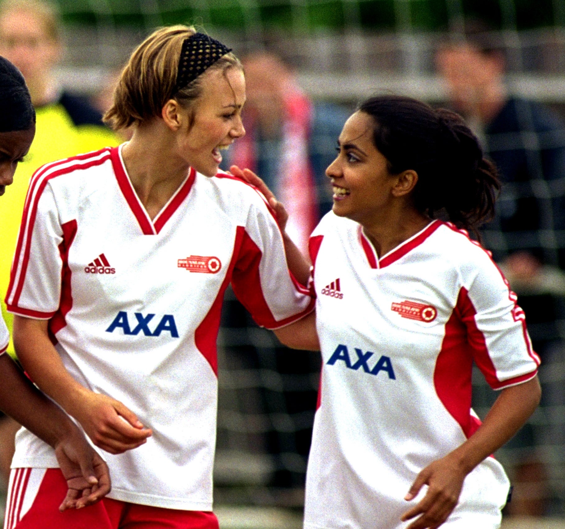 Two soccer players in matching jerseys celebrate on the field, smiling and embracing each other