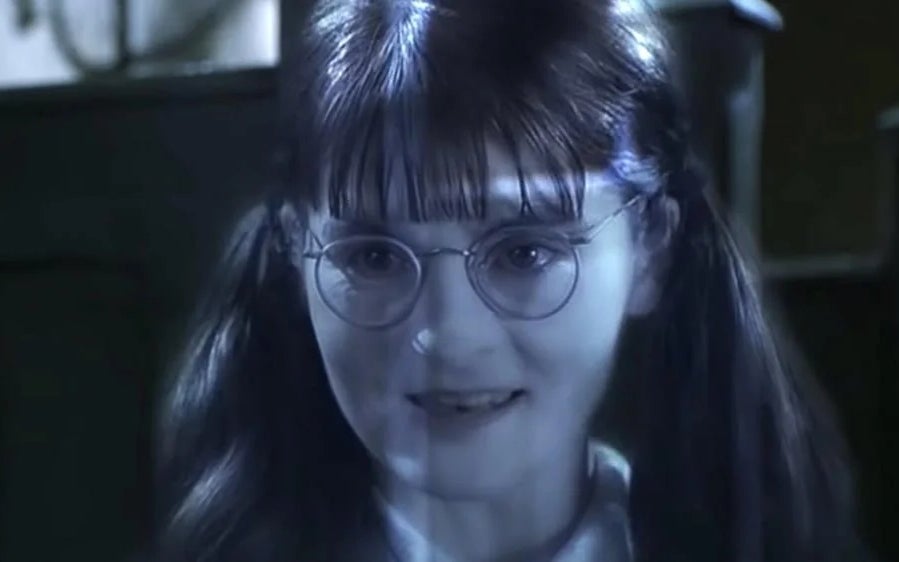 A person with glasses and pigtails, appearing as a translucent figure, smiles with a background of dark surroundings
