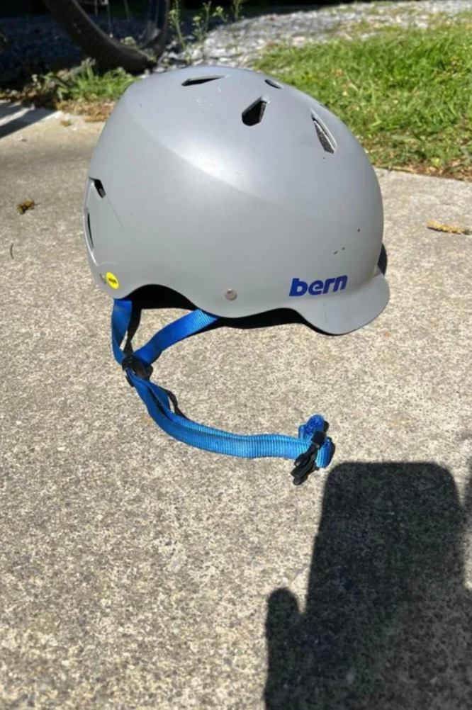 A bicycle helmet on a concrete surface with a blue chin strap