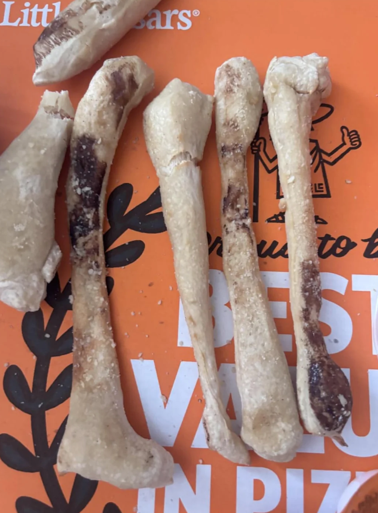 Five dog chew bones with dark spots lie on an orange surface