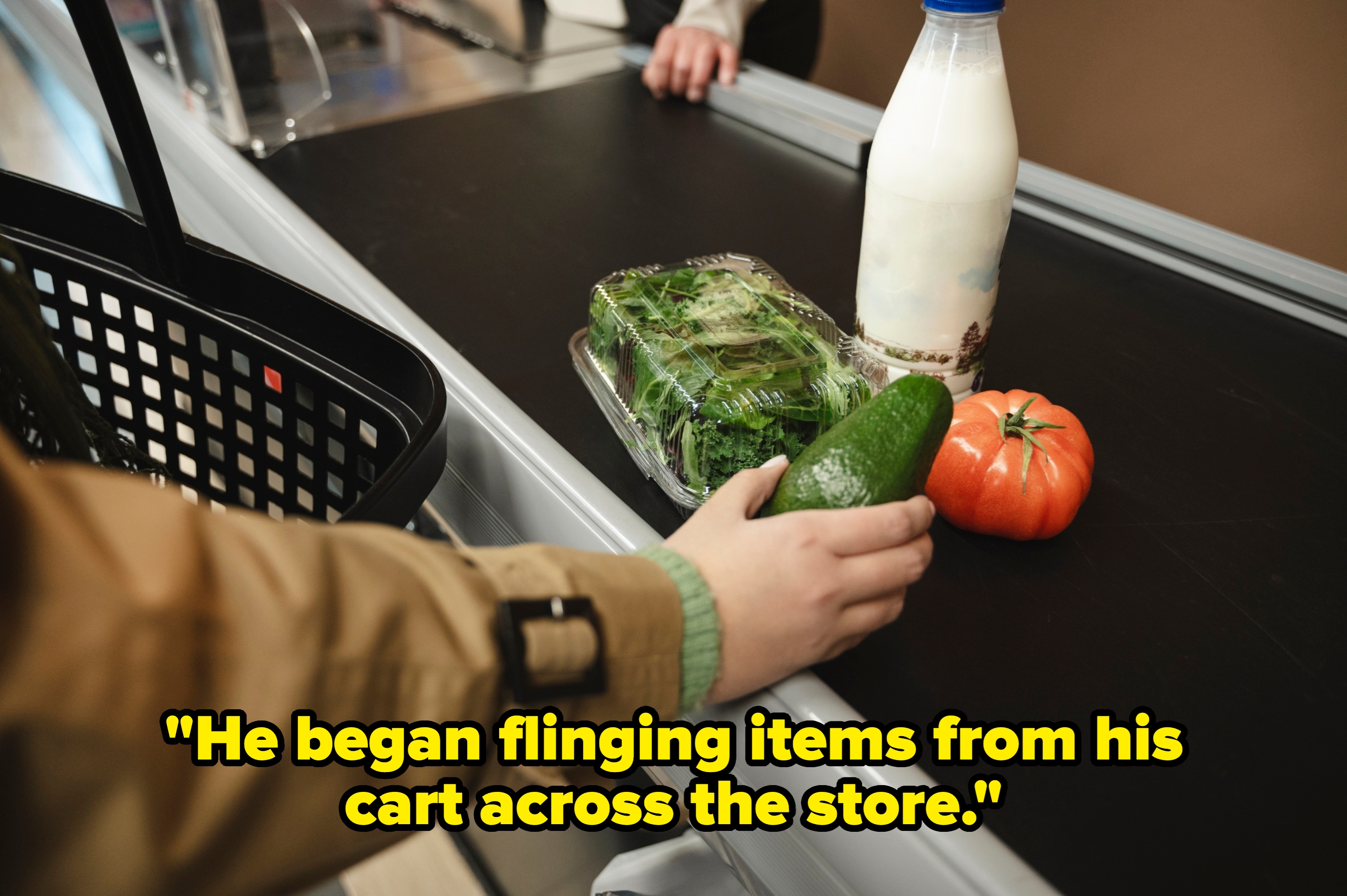 Grocery checkout conveyor with a hand placing avocado, packaged greens, a tomato, and a milk bottle