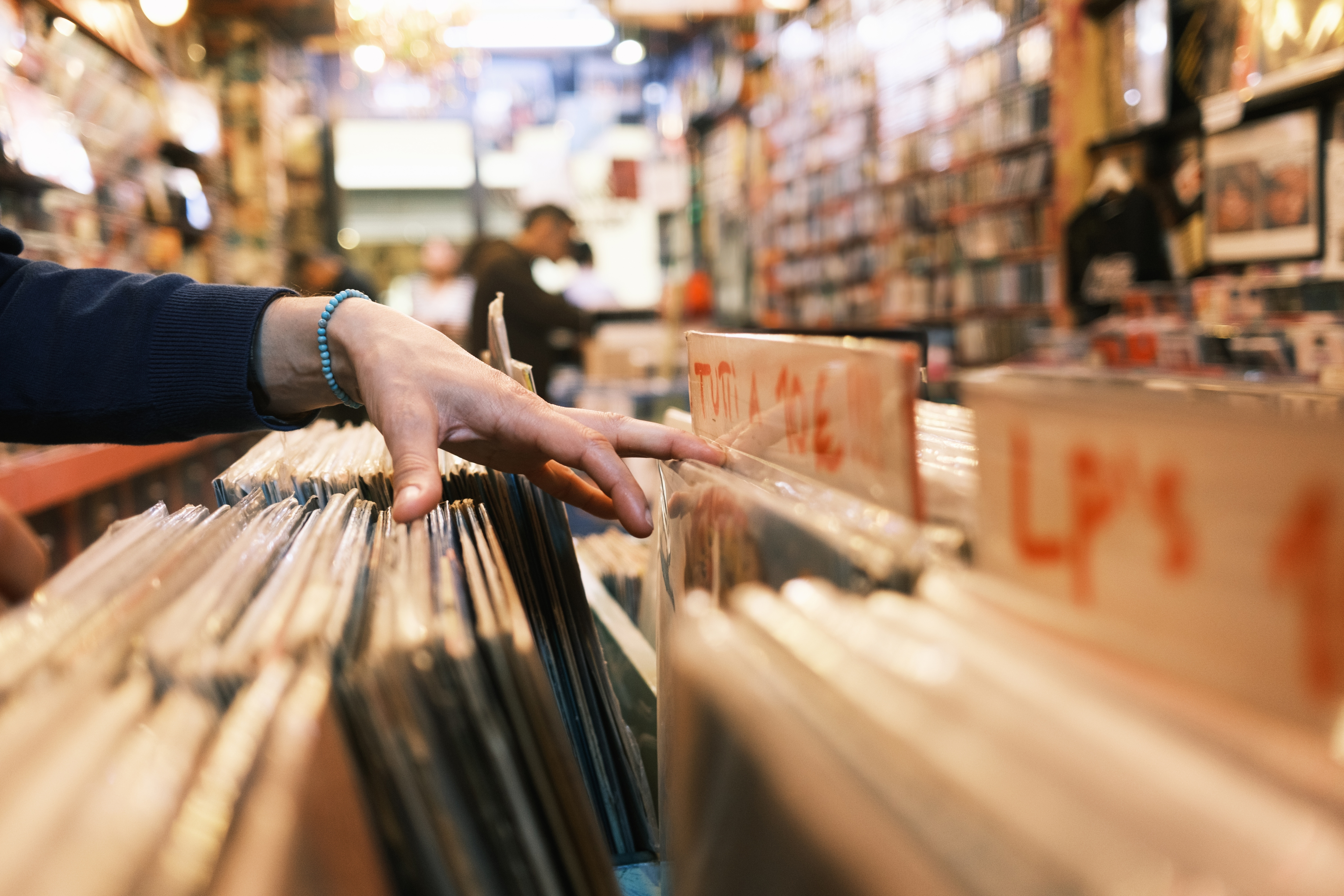 A person browsing through vinyl records in a busy store, with shelves full of albums in the background