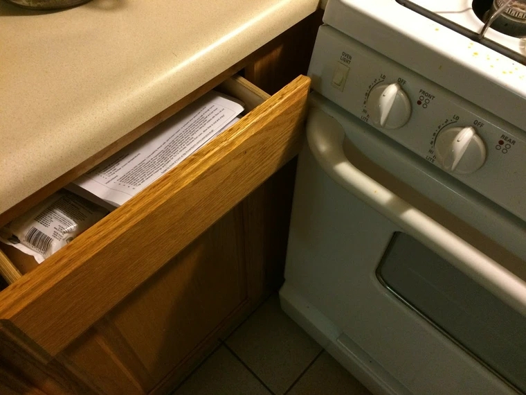 Kitchen drawer slightly open, blocked from opening further by oven handle