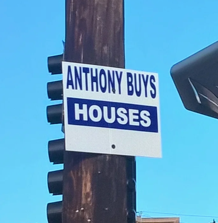 Sign on a traffic light post reads "Anthony Buys Houses."