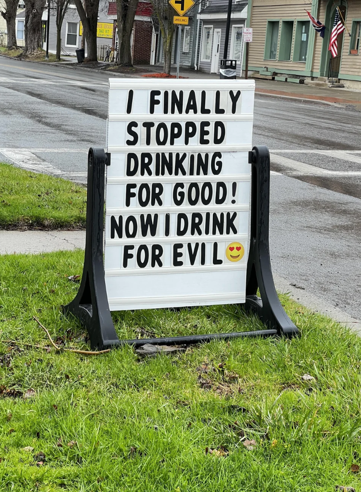 Sign on grass reads, "I finally stopped drinking for good! Now I drink for evil," with a smiling face emoji