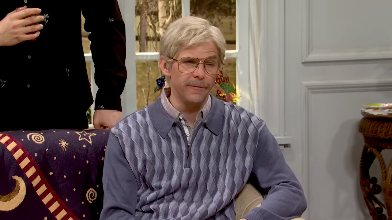 Person wearing a patterned sweater and glasses sits on a couch with a celestial-themed blanket in a living room setting