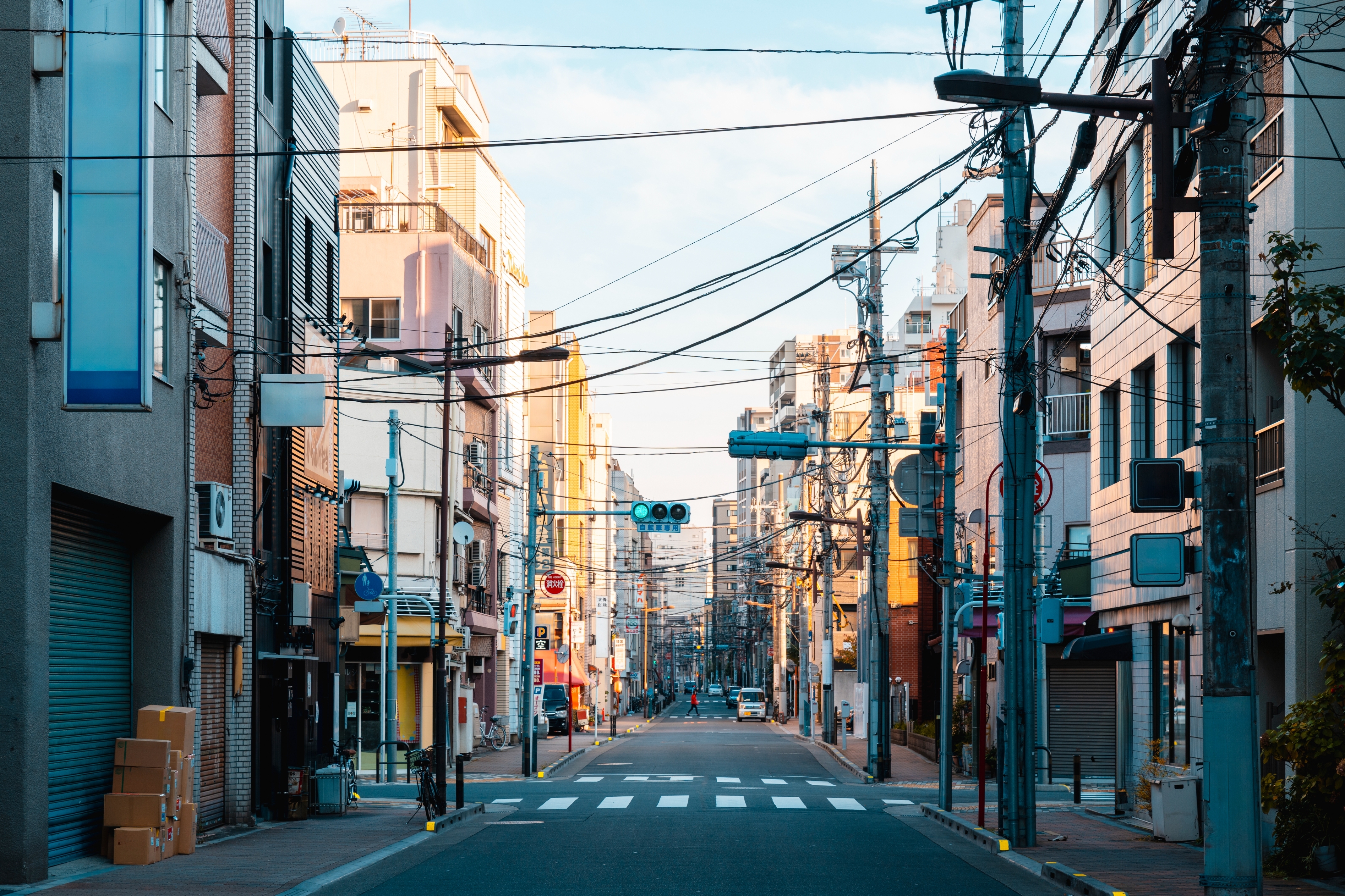 City street with overhead cables, lined with buildings and shops, suggesting a lively urban environment. The street is empty, conveying early morning calm