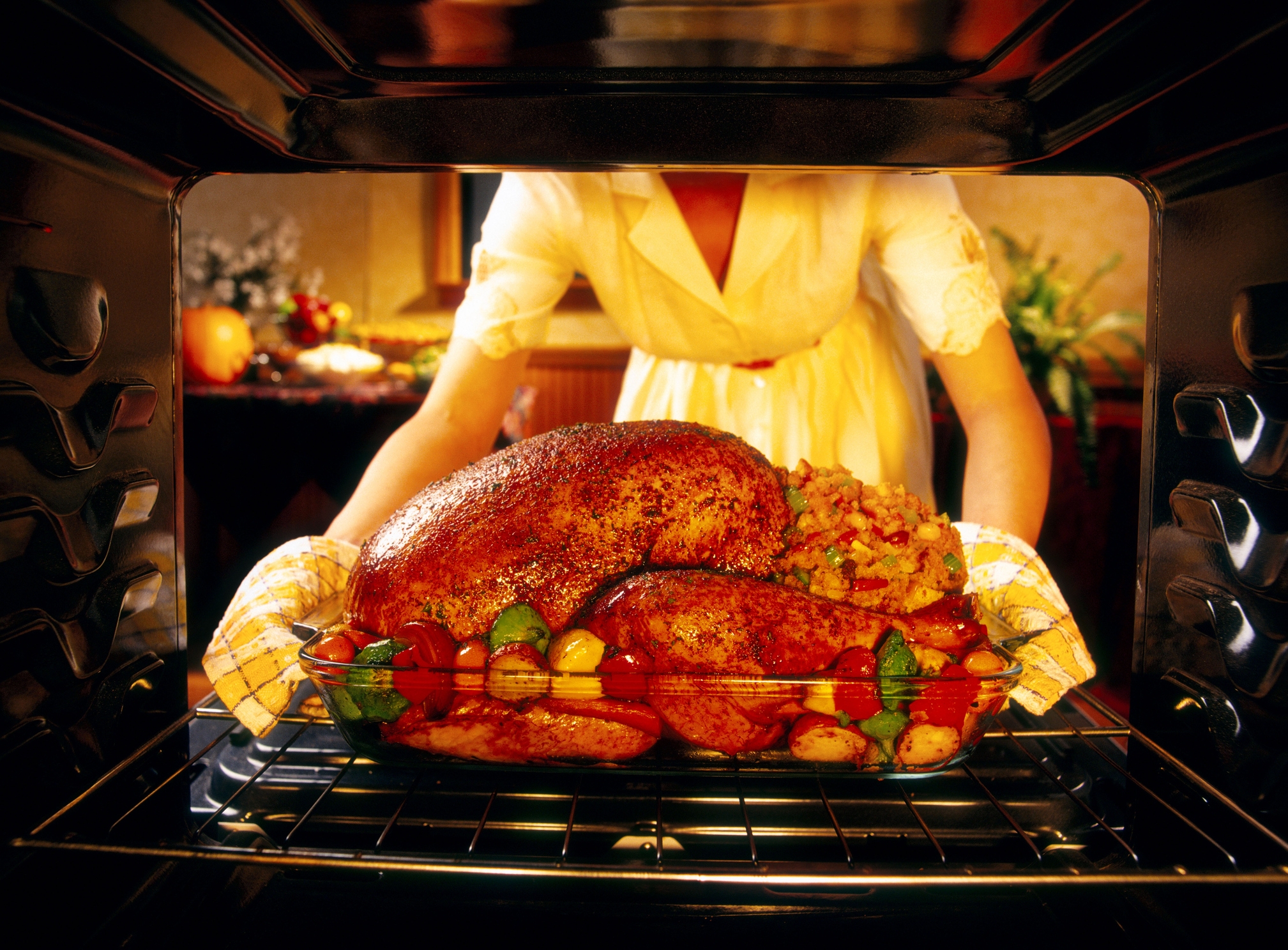Person placing a roasted turkey with vegetables into an oven, showcasing a festive meal preparation