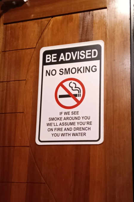 Sign on wooden door reads: "Be advised, no smoking. If we see smoke around you, we'll assume you're on fire and drench you with water."