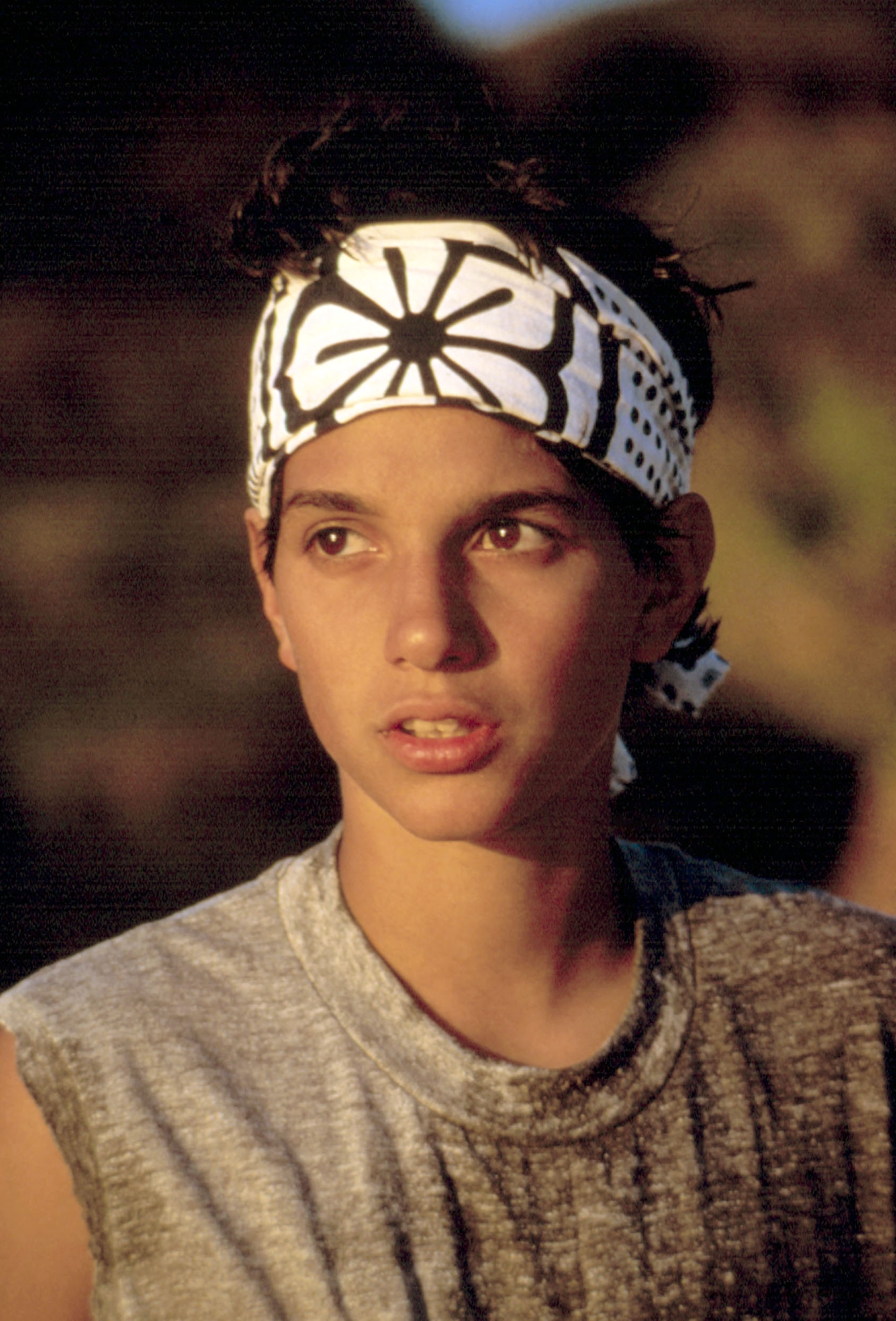 Person wearing a sleeveless shirt and a patterned headband, gazing thoughtfully into the distance