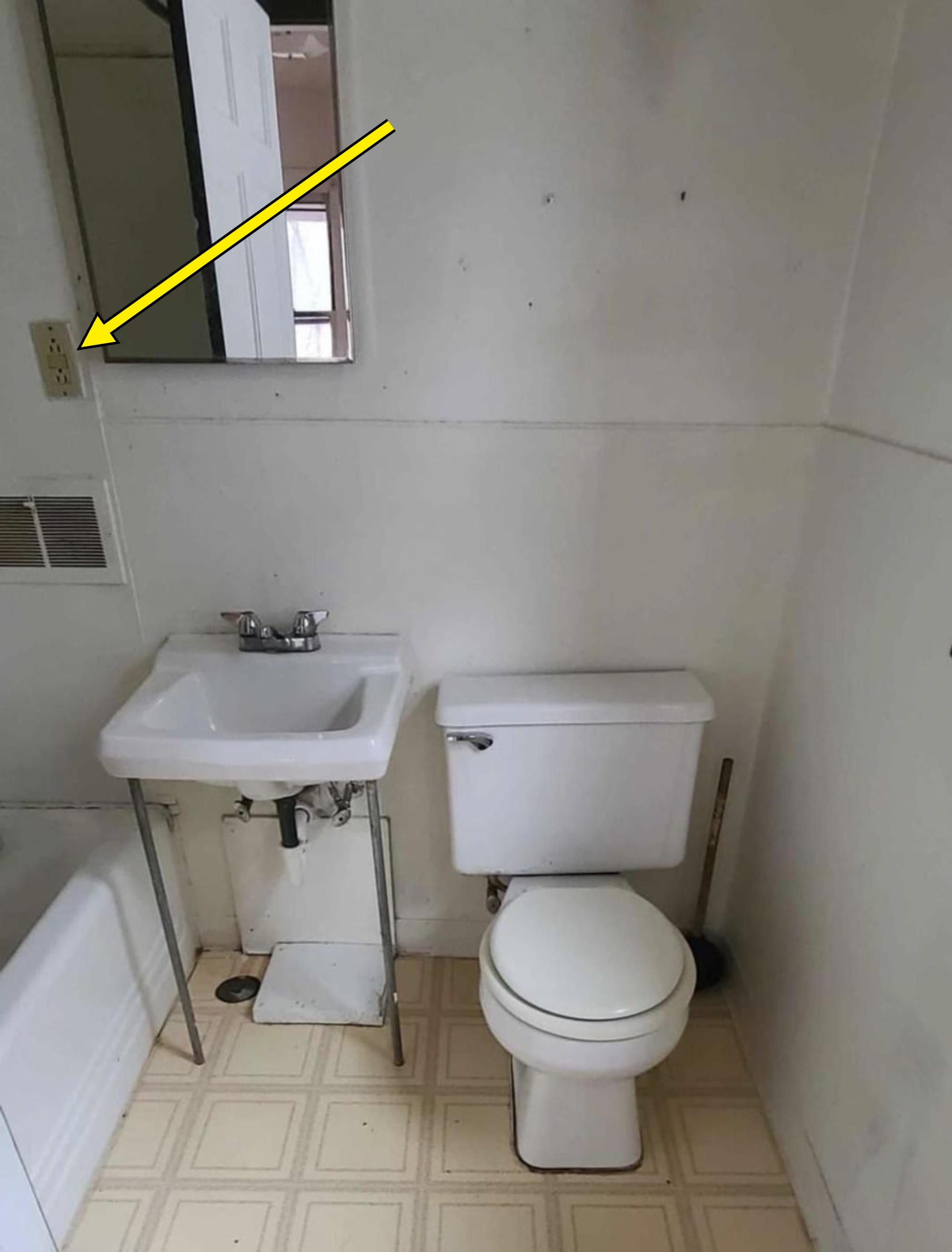 Small bathroom with toilet and sink. Arrow points to an electrical outlet in the shower