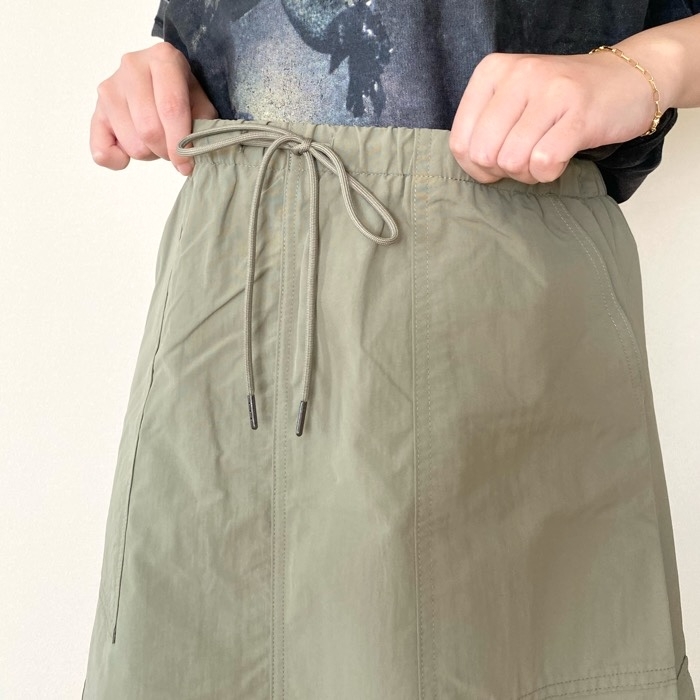 Person adjusting the drawstring on a casual skirt, wearing a graphic T-shirt, with hands partially visible