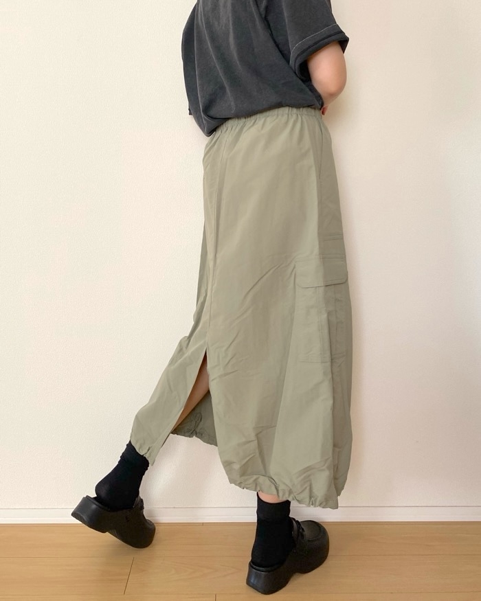 Person wearing a long, casual skirt with side slits and chunky shoes, standing against a plain wall