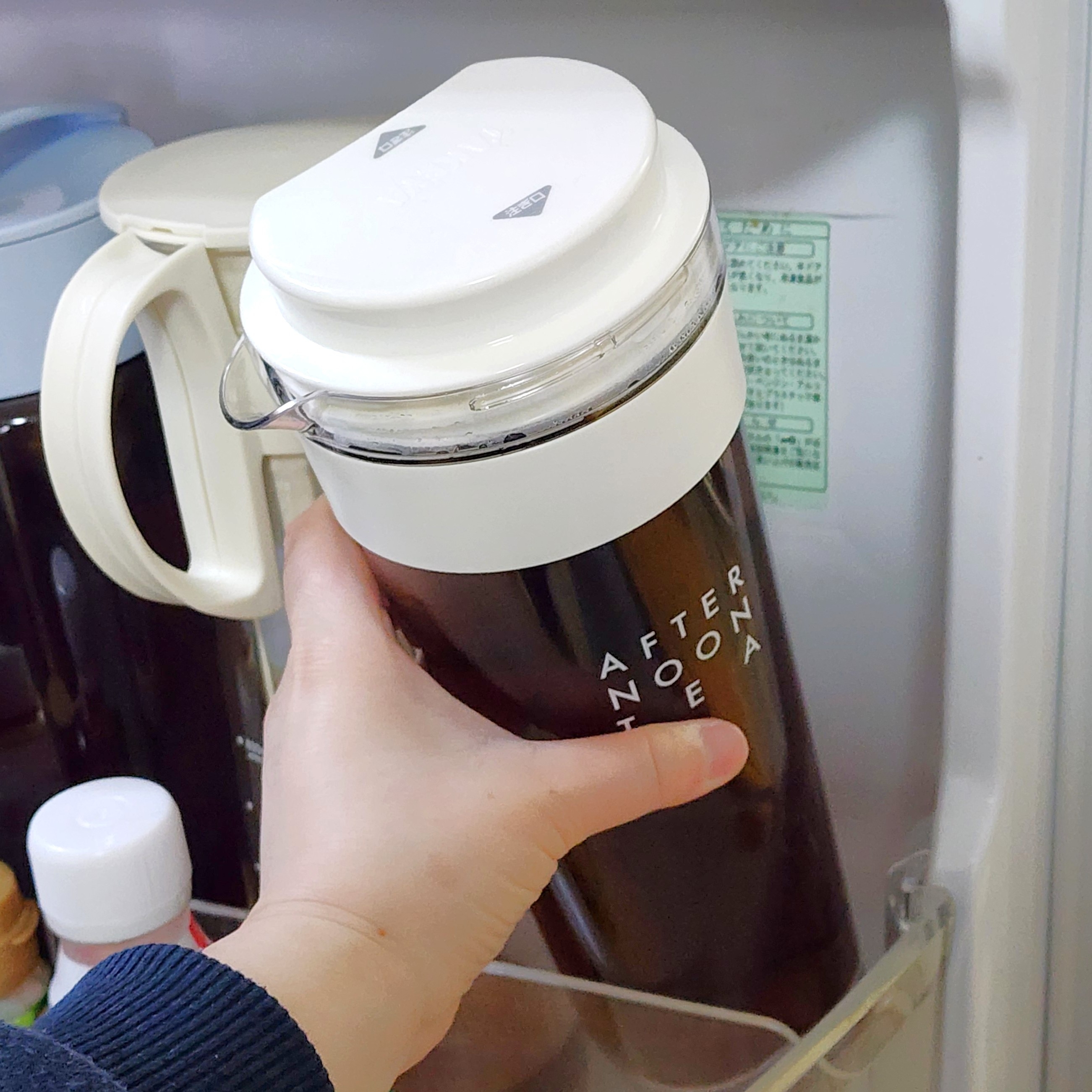 冷蔵庫内で手が蓋付きボトルを取り出そうとしている。ボトルには「AFTERNOON TEA」とプリントされている。
