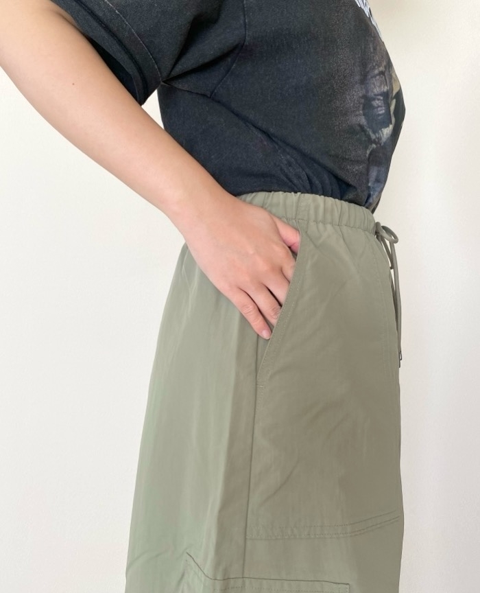 Person wearing casual T-shirt and high-waisted, drawstring pants with hands in pocket, standing against plain background