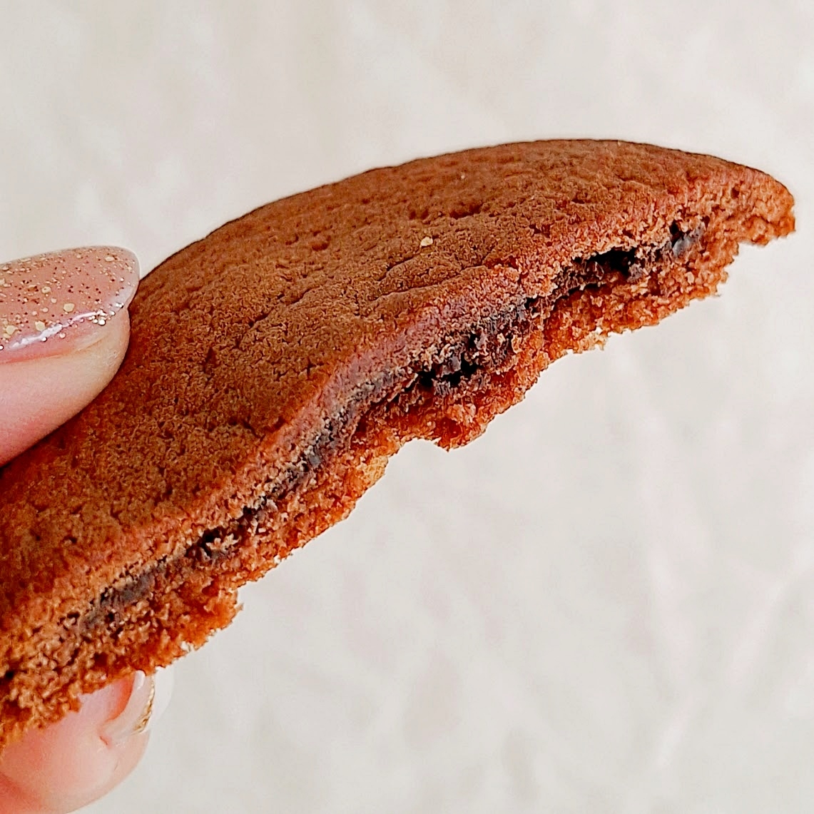 クッキーの断面図。手で持たれており、中にチョコレートのようなフィリングが見えるシンプルなお菓子。