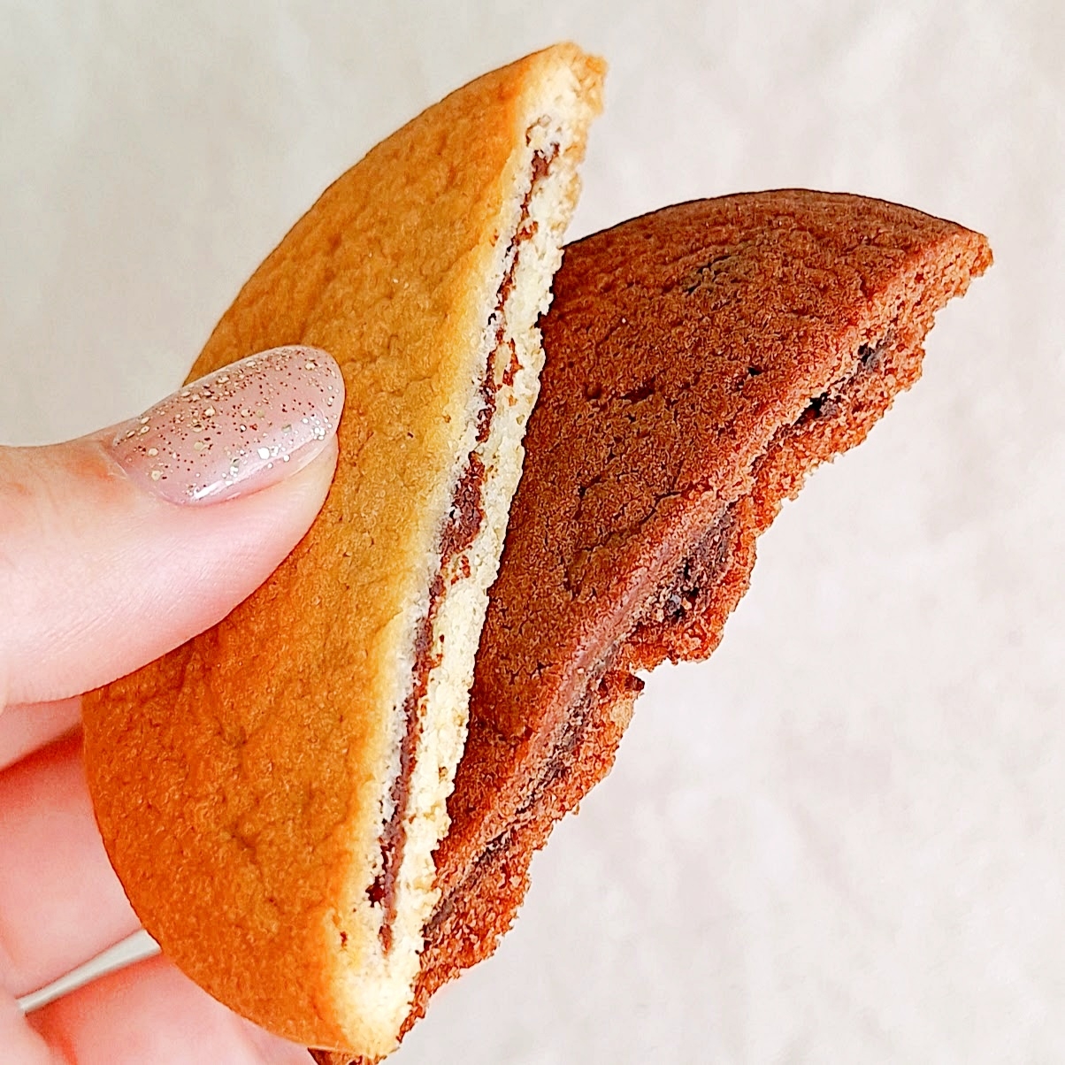 手に持たれた柔らかそうなクッキー。外側が焼き色の異なる二層になっていて、真ん中にチョコレートが挟まれている。