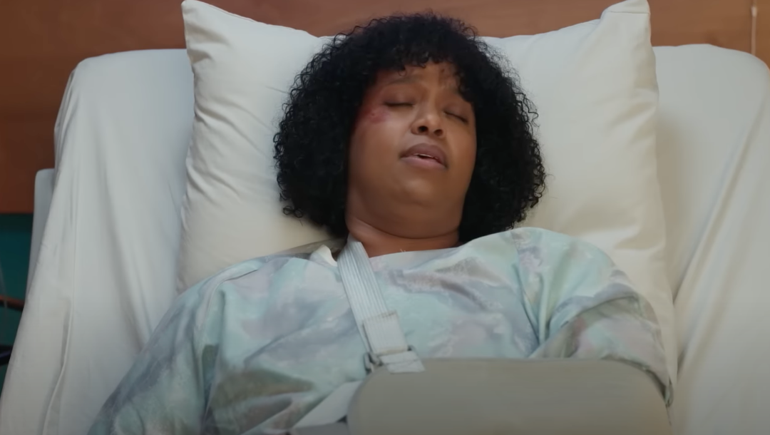 A person rests in a hospital bed with a sling on their arm and a visible bruise, suggesting a recovery scene