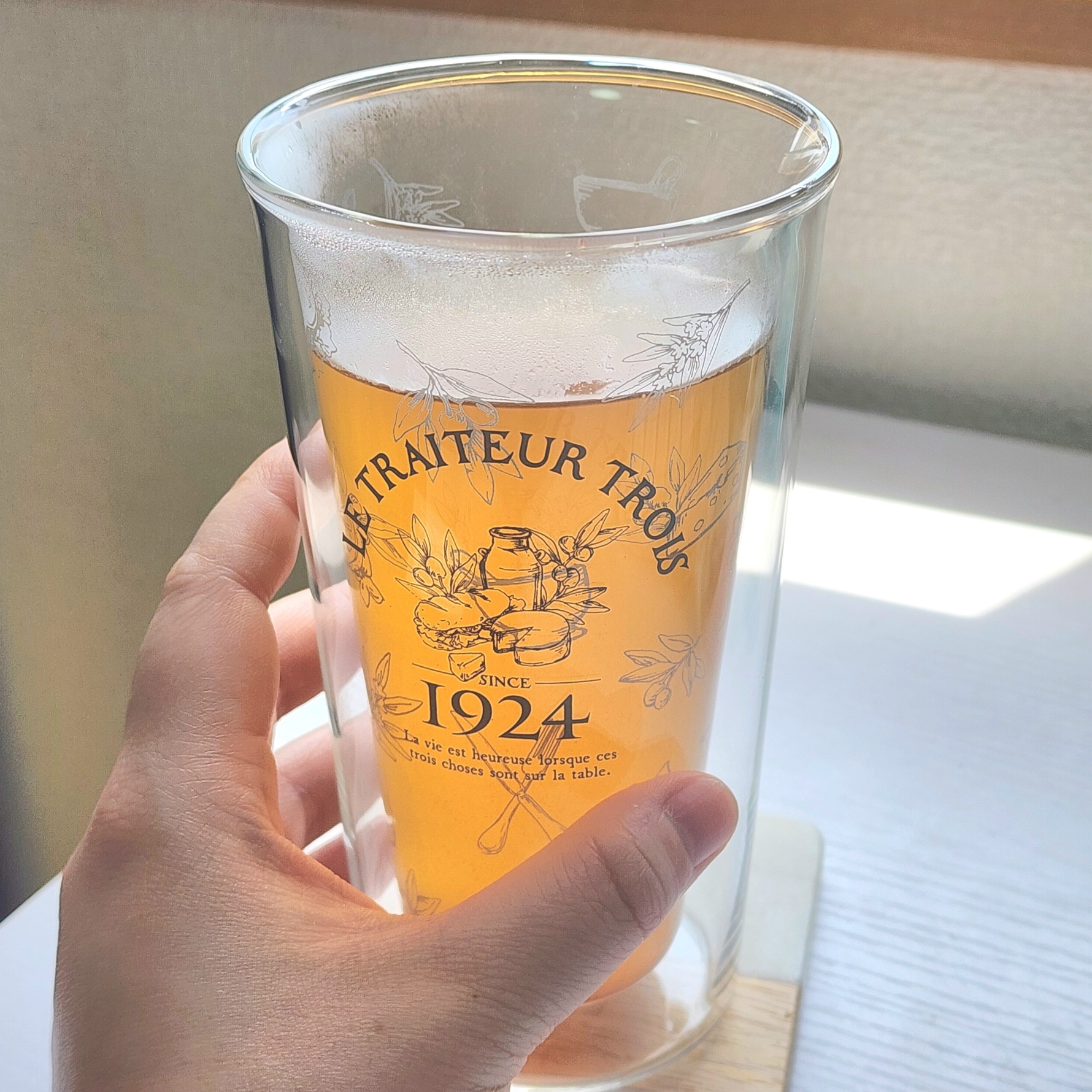 透明グラスを手に持っている人。グラスには「1924」などの文字が印刷され、淡い色のビールが入っています。