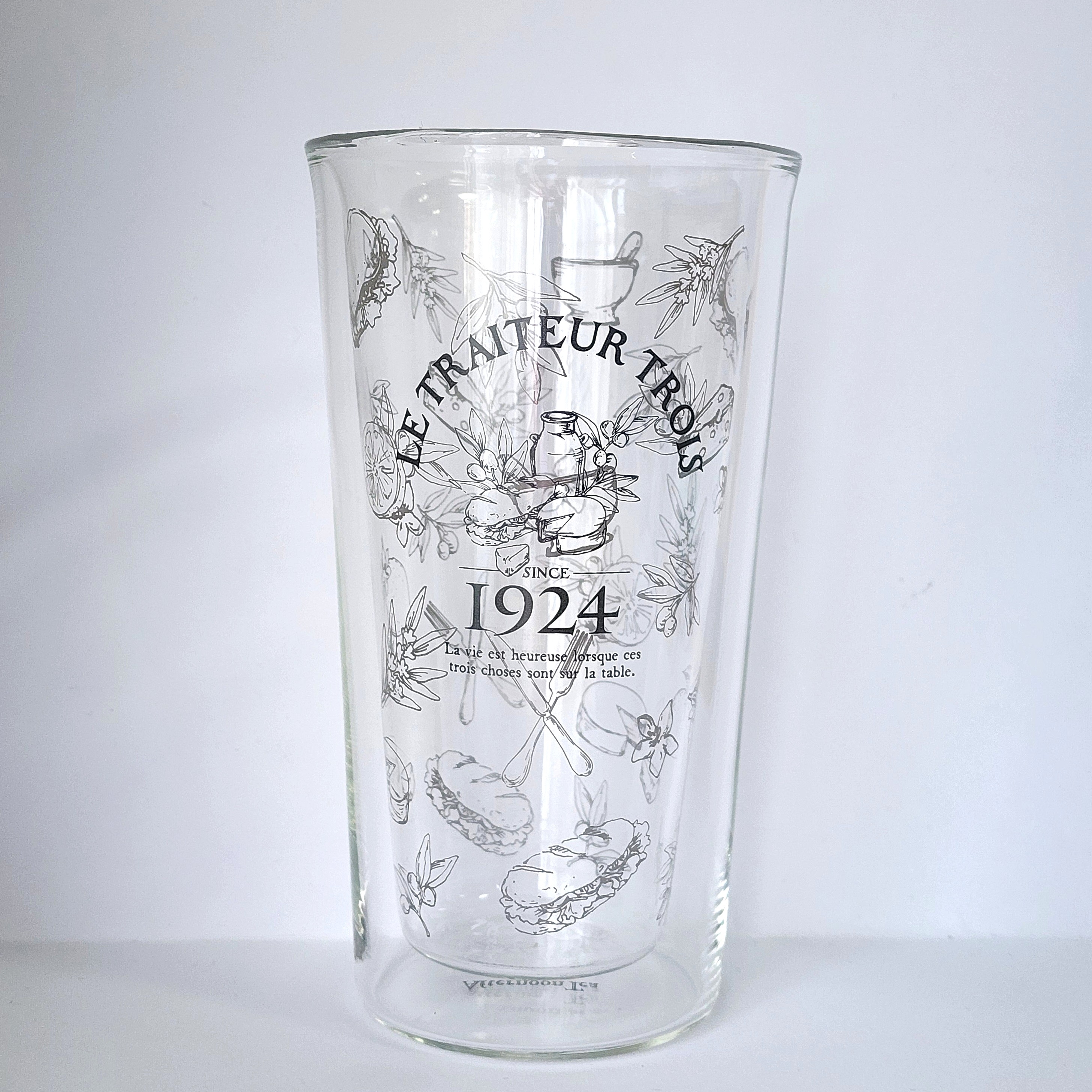 イラストとフランス語のテキストが描かれたガラスのコップ。「1924」と書かれている。