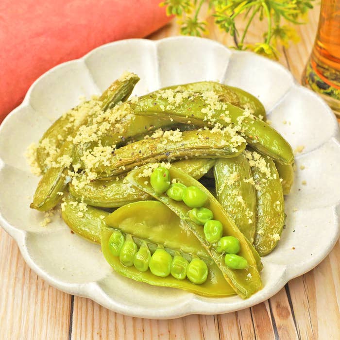 焼いたスナップエンドウが白い皿に盛られている。そばにチーズのようなものがかかっている。